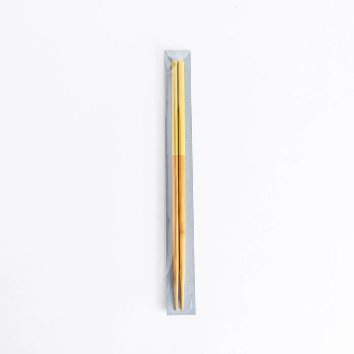 Yellow-tipped cooking chopsticks in sealed packaging, wooden stems visible, set on a neutral background.