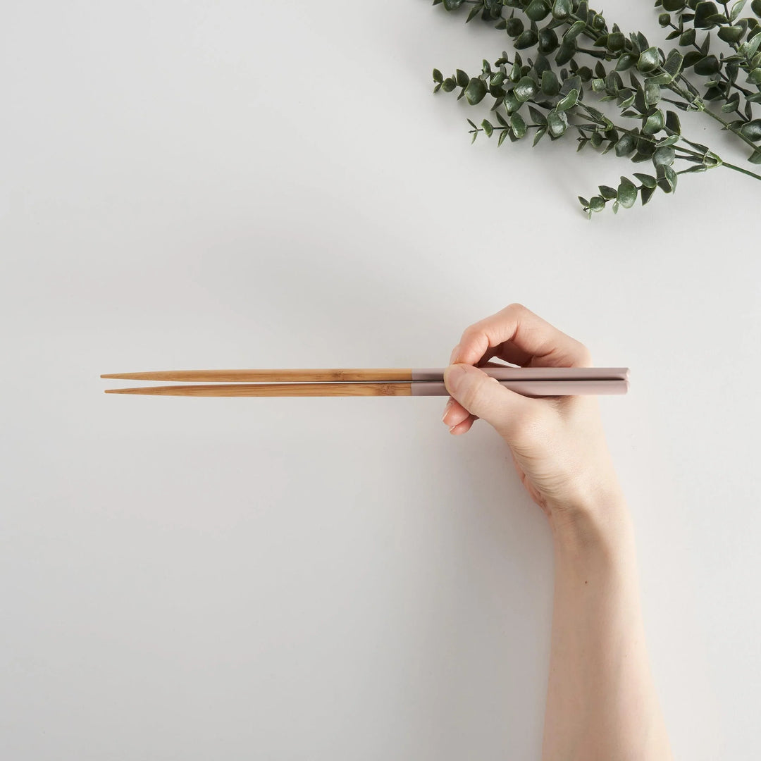 Chopsticks being held in hand, displaying light pink tips with a bamboo finish on the rest of the length.