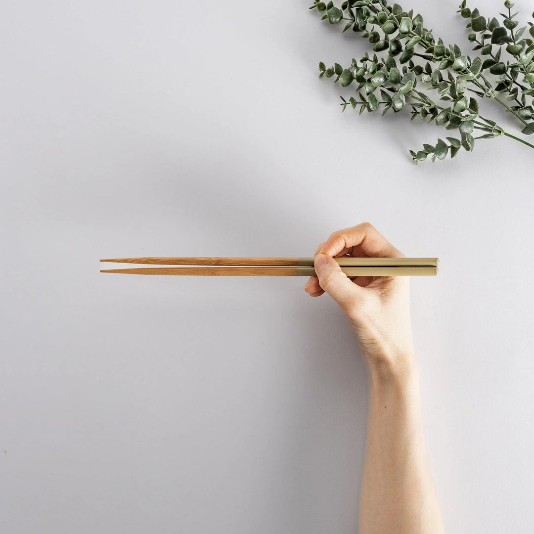 A hand holding beige-tipped bamboo cooking chopsticks, ideal for easy and comfortable food handling.