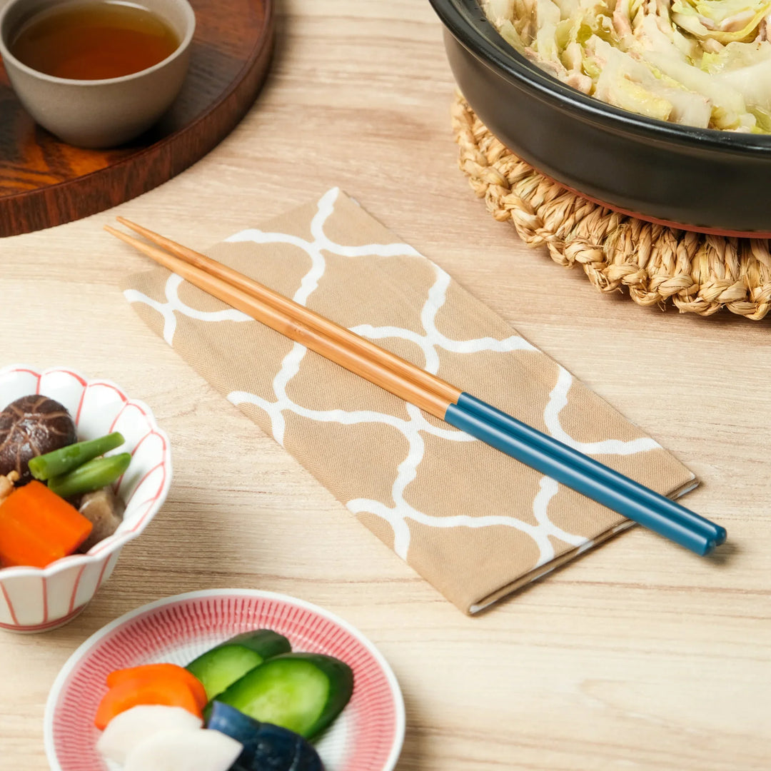 Teal and natural wood Japanese cooking chopsticks beside pickles simmered vegetables and hot pot on napkin.