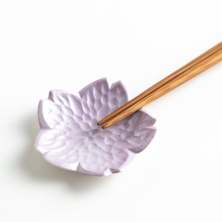 Small flower shaped chopstick rests in yellow blue white and pink arranged neatly on wooden surface.