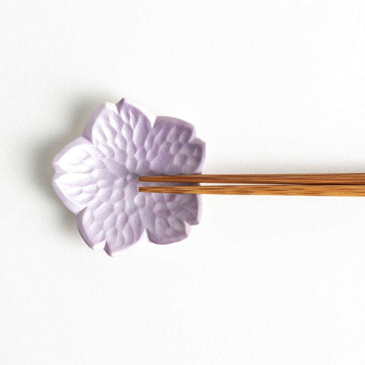 Small flower shaped chopstick rests in yellow blue white and pink arranged neatly on wooden surface.