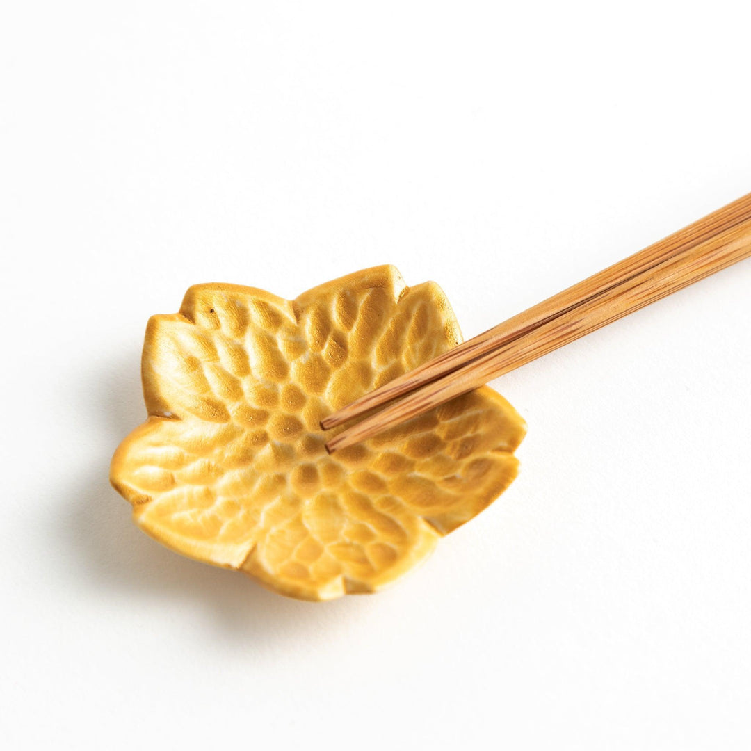 Small flower shaped chopstick rests in yellow blue white and pink arranged neatly on wooden surface.