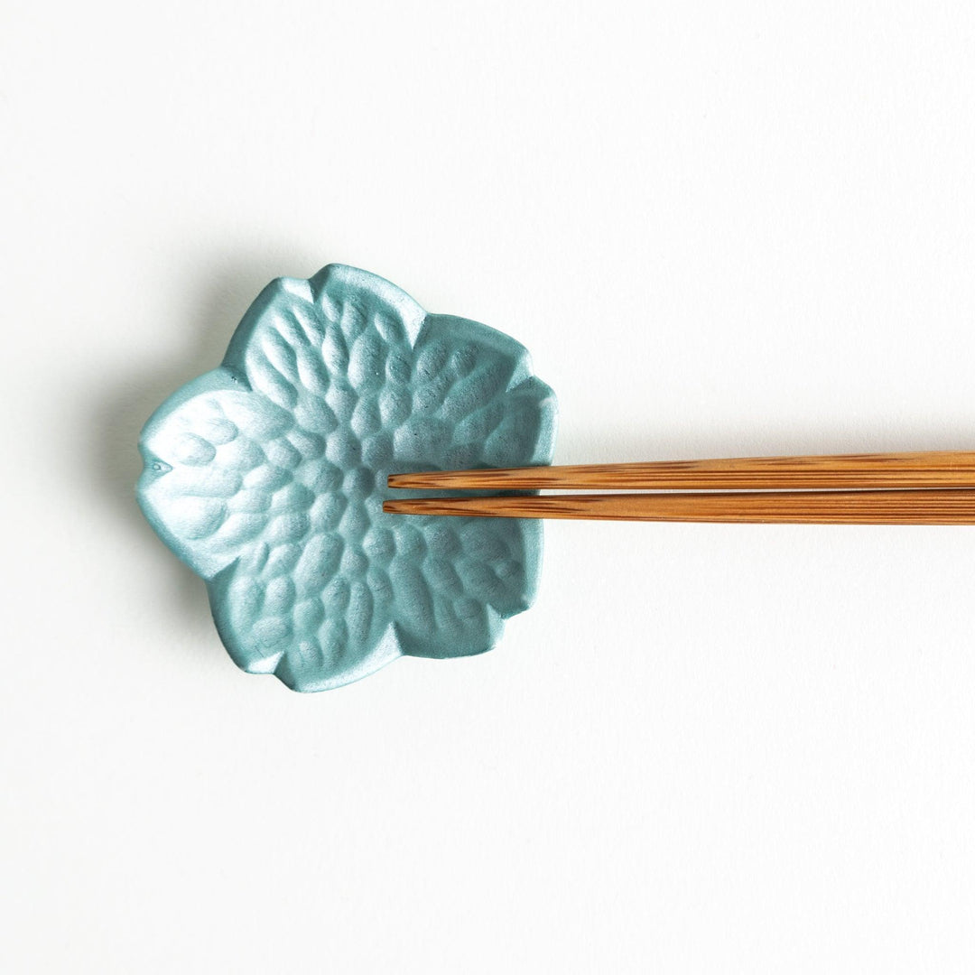Small flower shaped chopstick rests in yellow blue white and pink arranged neatly on wooden surface.