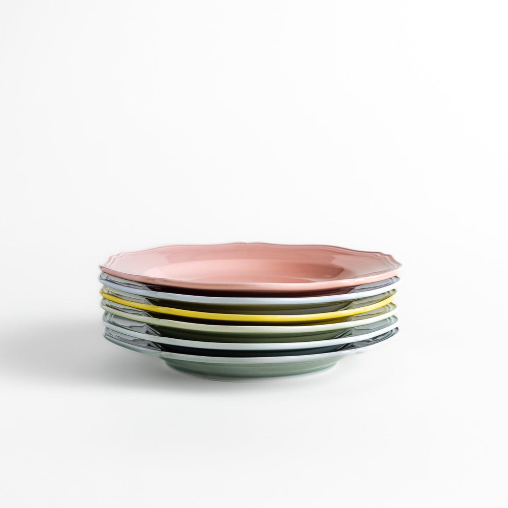 Stack of pastel ceramic dinner plates with scalloped edges in soft hues, combining everyday charm with refined design