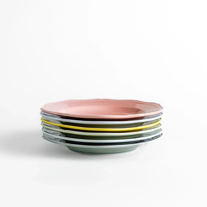 Stack of pastel ceramic dinner plates with scalloped edges in soft hues, combining everyday charm with refined design