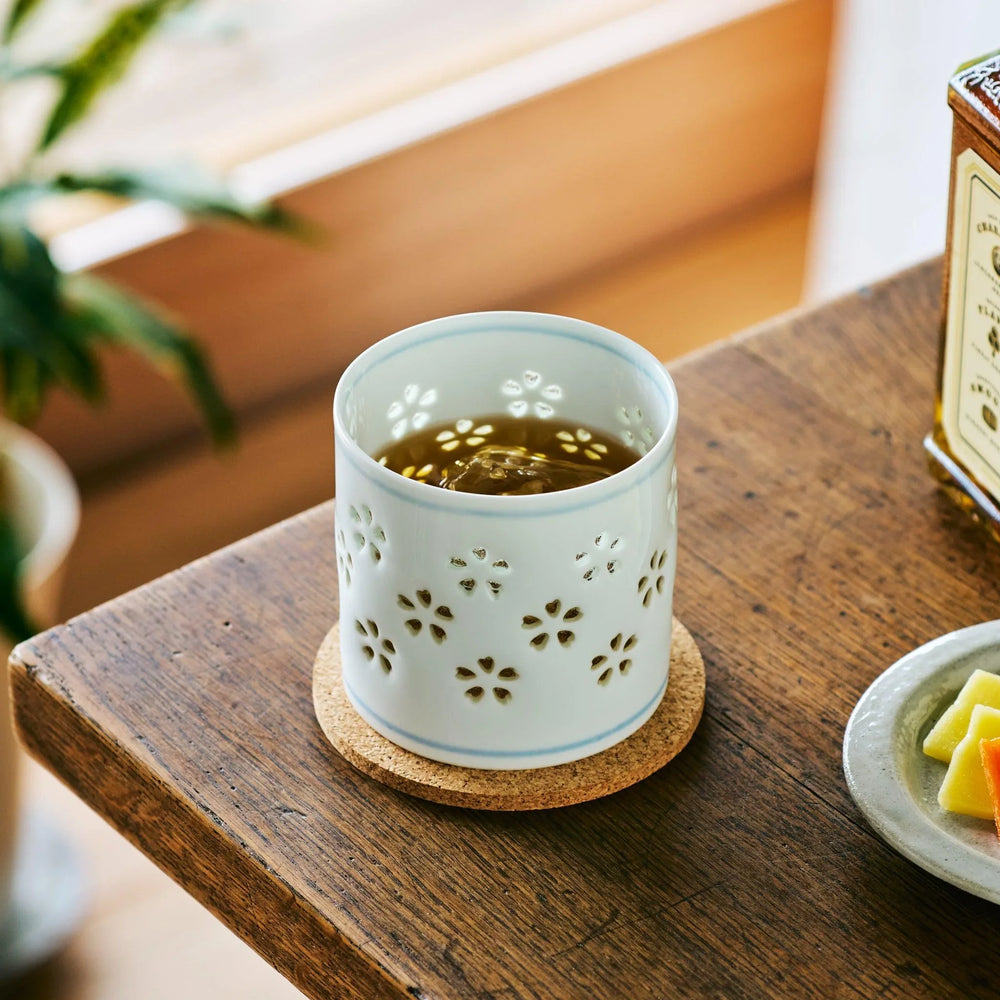 Japanese porcelain whiskey cup with sakura-shaped cutouts, filled with whiskey and resting in natural light.