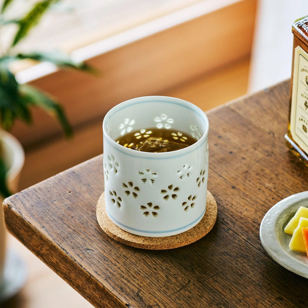 Japanese porcelain whiskey cup with sakura-shaped cutouts, filled with whiskey and resting in natural light.