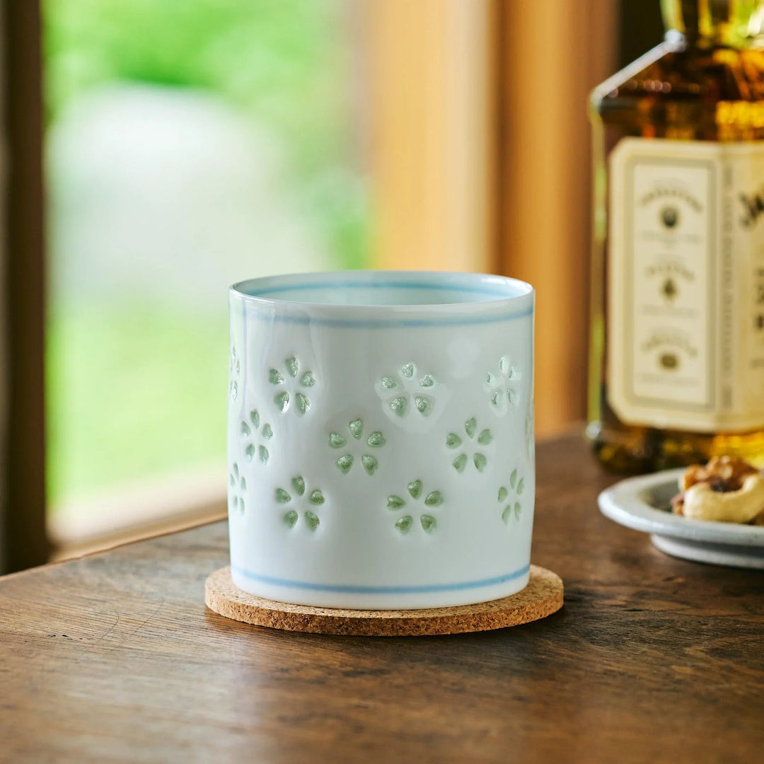 Petal Crystal Rocks Glass with a sakura cutout design, filled with whiskey and glowing green in the sunlight.