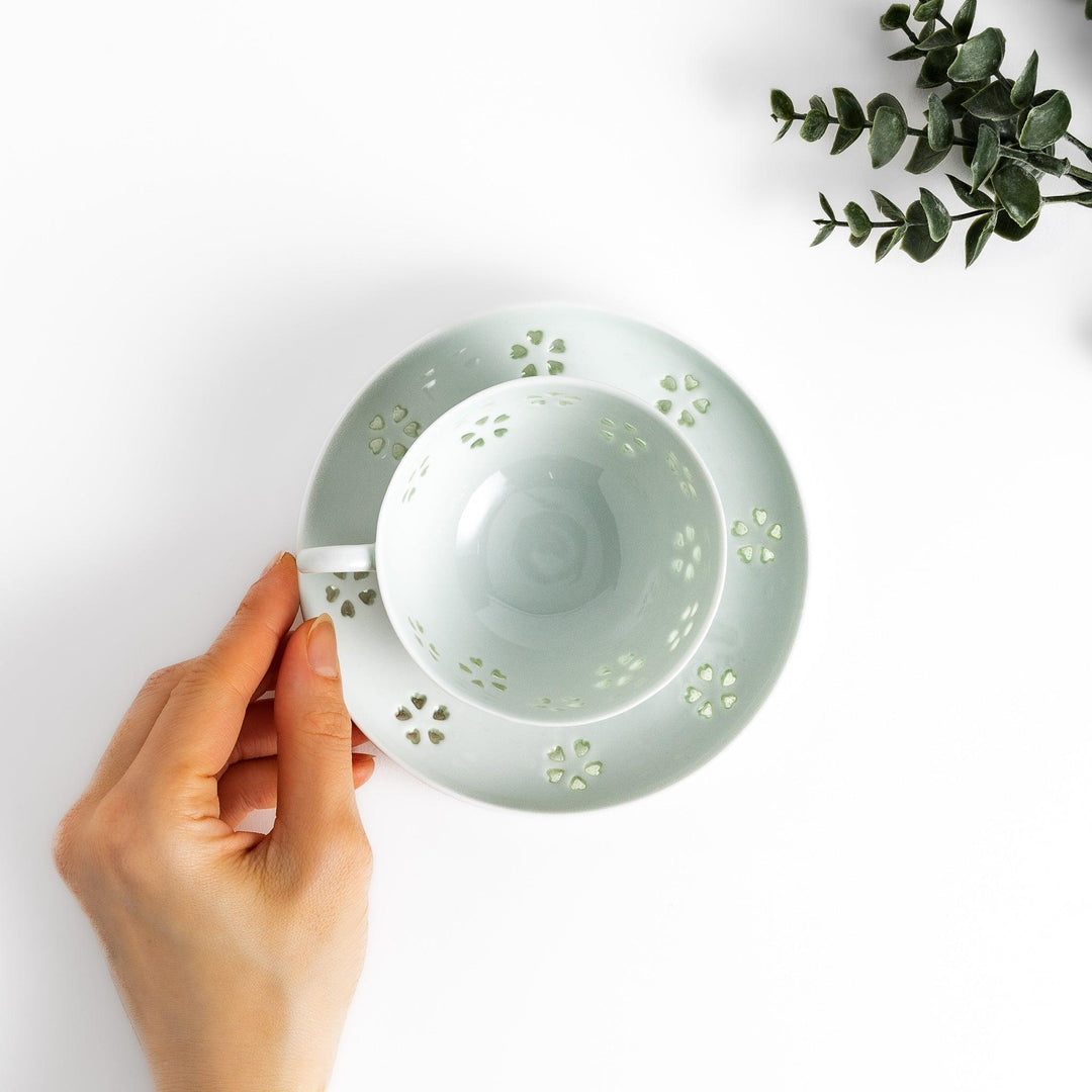 Delicate teacup and saucer set featuring intricate petal-shaped cutouts, allowing light to pass through, creating a soft, elegant design in pale green and white porcelain.