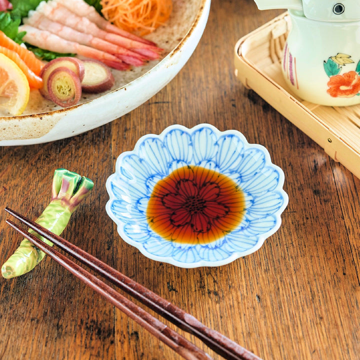 Scalloped sauce dish with vivid red and blue petal pattern soy sauce chopsticks and wasabi rest.