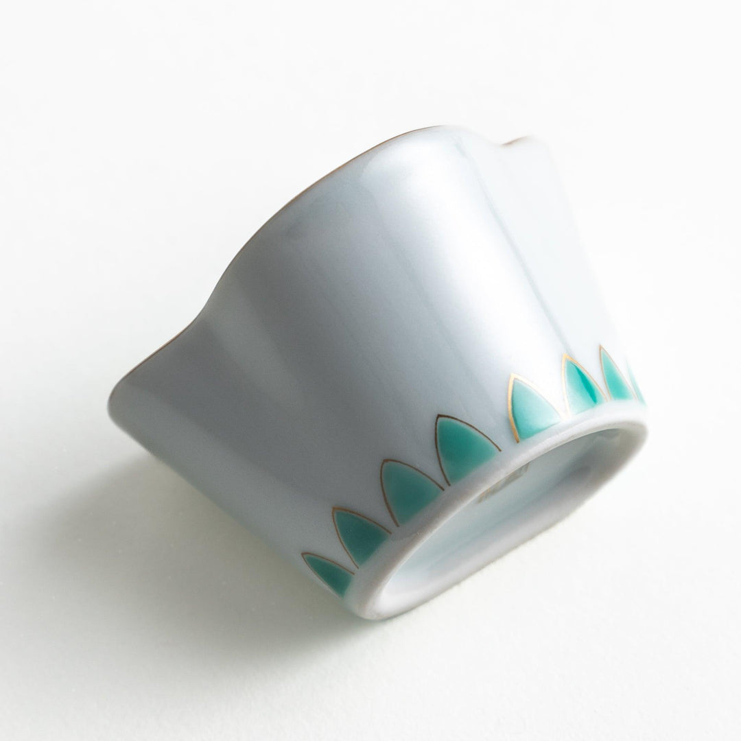 A small, white ceramic bowl with a green fan-like pattern and gold trim.