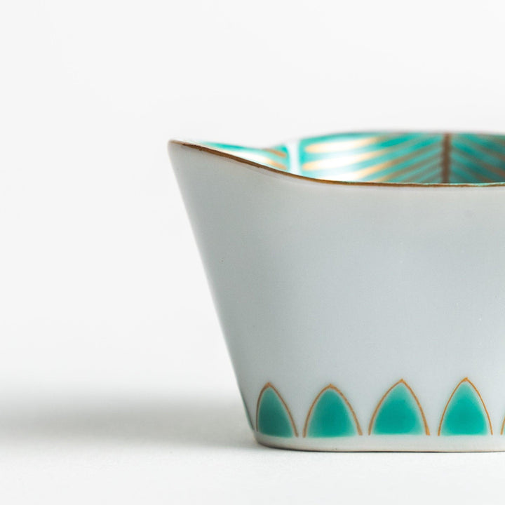 A small, white ceramic bowl with a green fan-like pattern and gold trim.