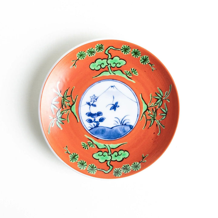 Round plate with an orange background, green leaves, and a Mount Fuji scene.