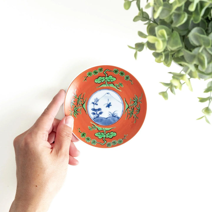 Round plate with an orange background, green leaves, and a Mount Fuji scene.