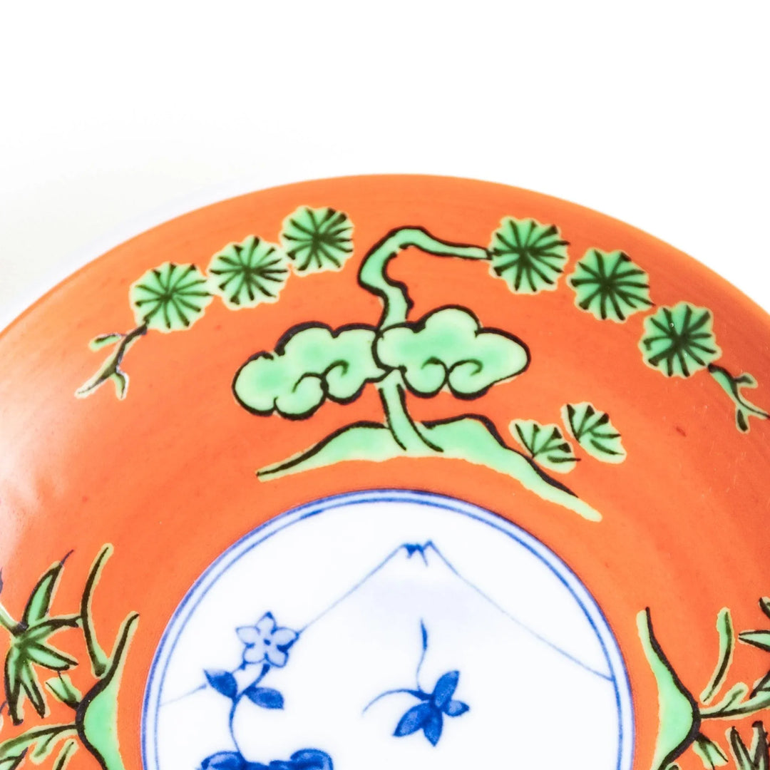 Round plate with an orange background, green leaves, and a Mount Fuji scene.