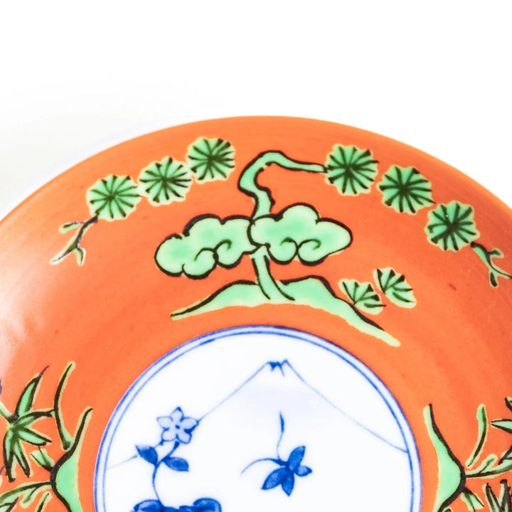 Round plate with an orange background, green leaves, and a Mount Fuji scene.