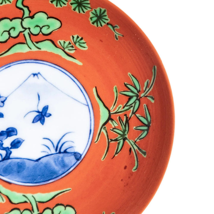 Round plate with an orange background, green leaves, and a Mount Fuji scene.