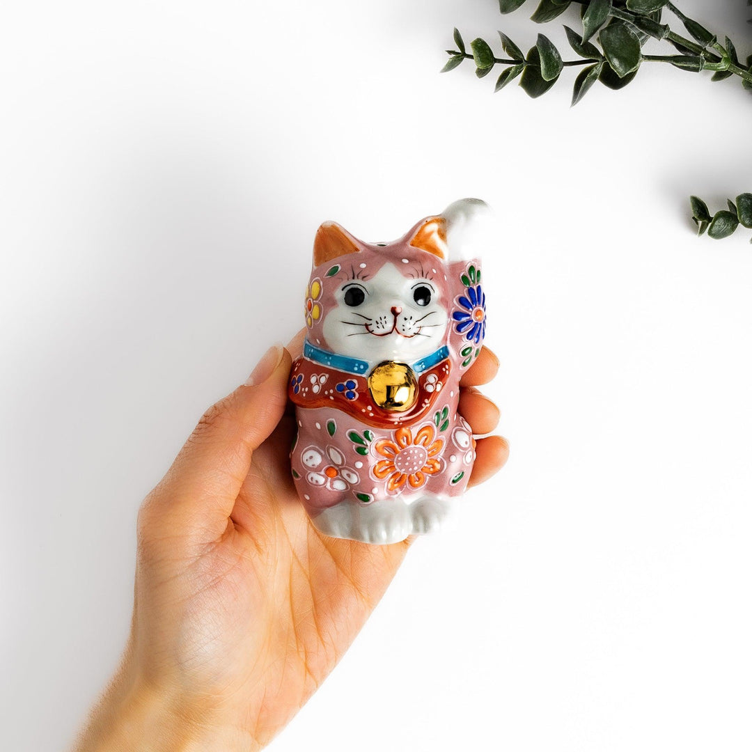 Pink blossom Maneki Neko figurine with floral patterns and gold bell symbolizing good luck and prosperity.