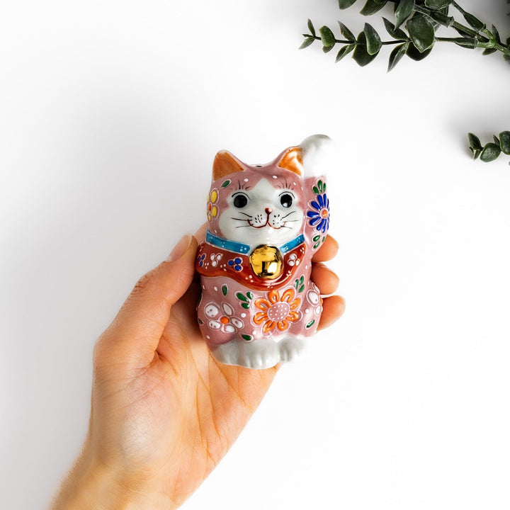 Pink blossom Maneki Neko figurine with floral patterns and gold bell symbolizing good luck and prosperity.