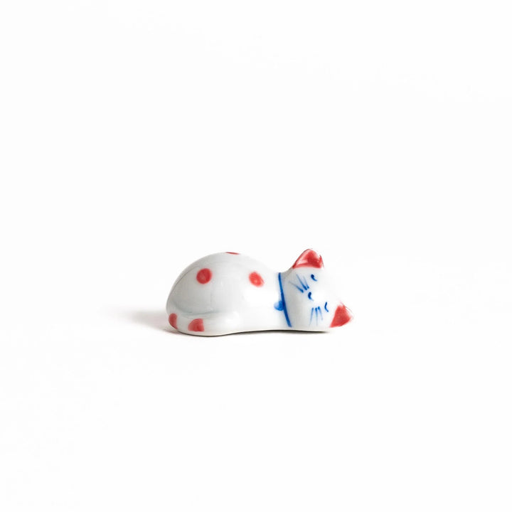 Adorable white ceramic chopstick rest shaped like a sleeping cat with red dots, adding a playful touch to your table setting.