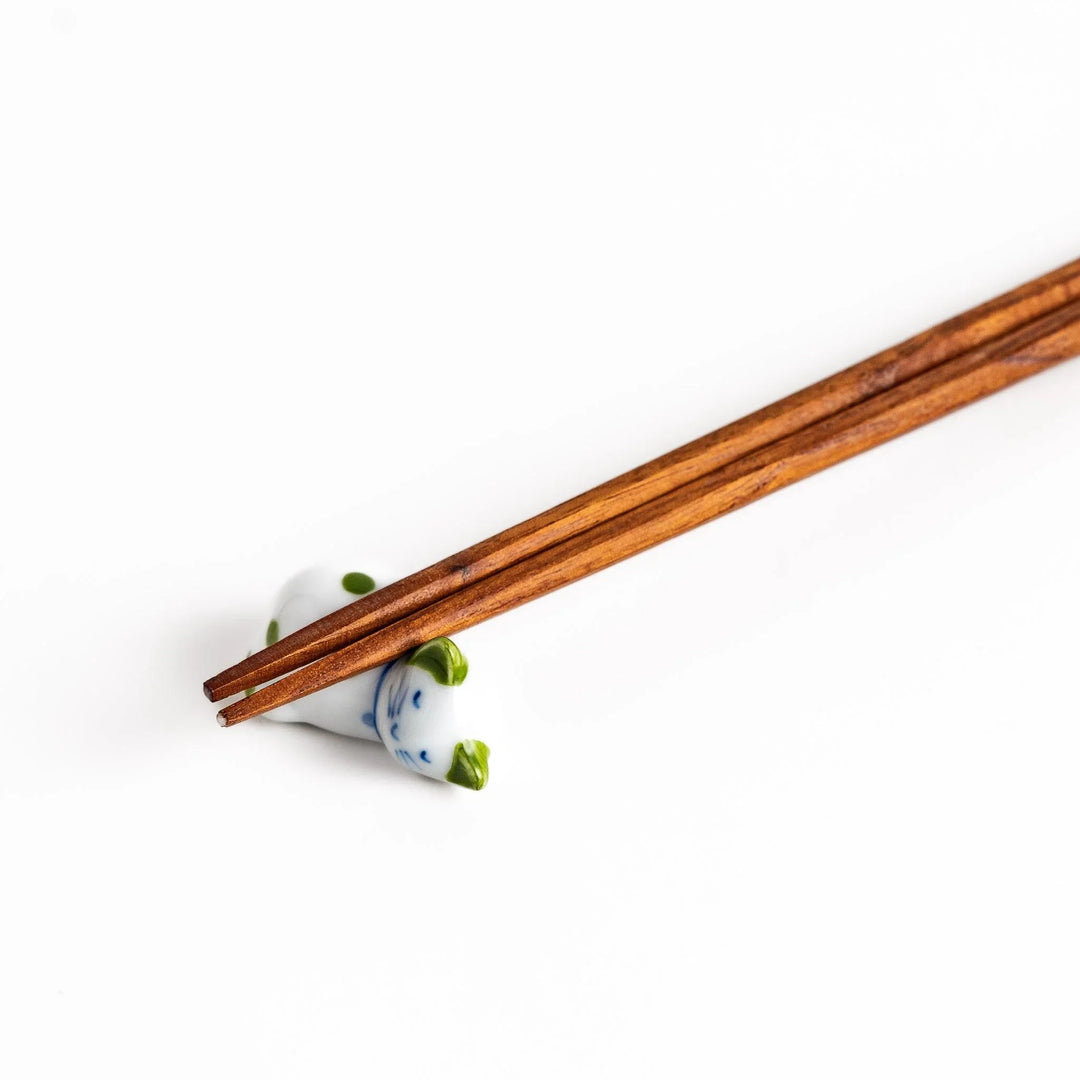 Wooden chopsticks on white ceramic sleeping cat chopstick rest with green dots for charming setting.