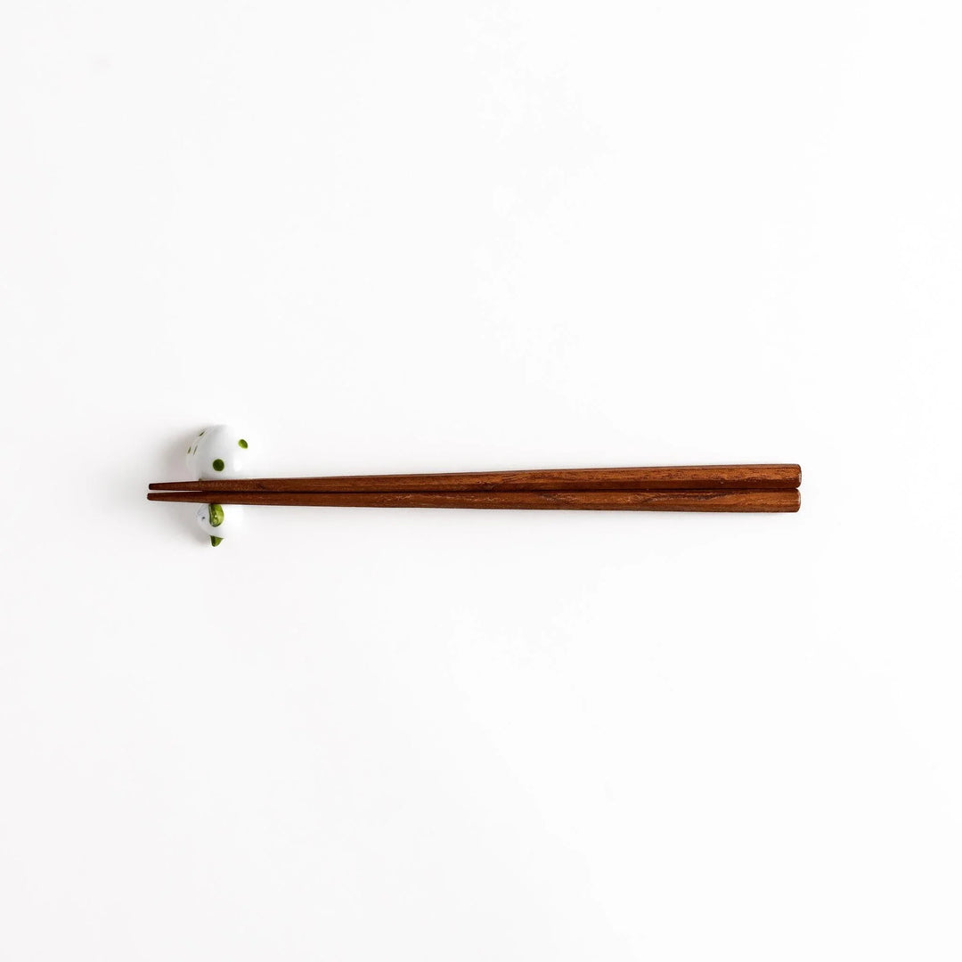 Wooden chopsticks on white ceramic sleeping cat chopstick rest with green dots for charming setting.