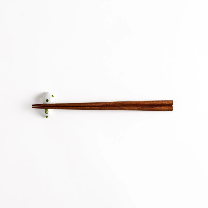 Wooden chopsticks on white ceramic sleeping cat chopstick rest with green dots for charming setting.