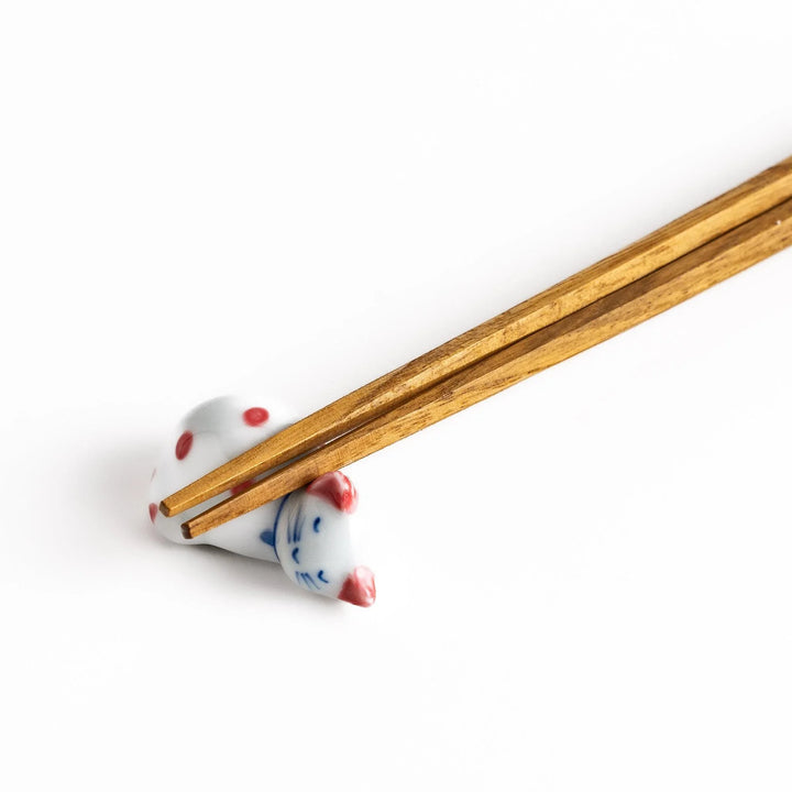 Wooden chopsticks resting on an adorable white ceramic chopstick rest shaped like a sleeping cat with red dots.