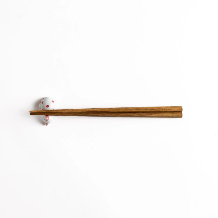 Wooden chopsticks resting on an adorable white ceramic chopstick rest shaped like a sleeping cat with red dots.