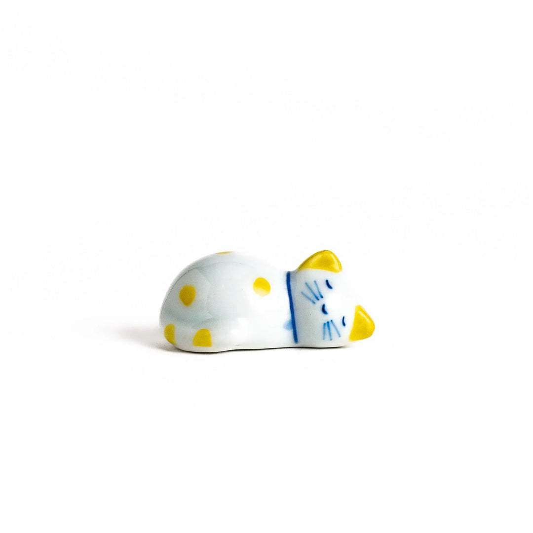 White ceramic cat chopstick rest with yellow dots in sleeping pose adding cheerful touch to dining.
