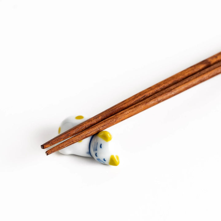 Wooden chopsticks resting on a charming white ceramic chopstick rest shaped like a sleeping cat with yellow dots.