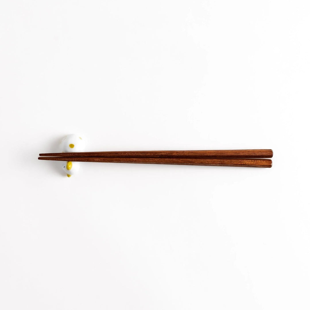 Wooden chopsticks resting on a charming white ceramic chopstick rest shaped like a sleeping cat with yellow dots.