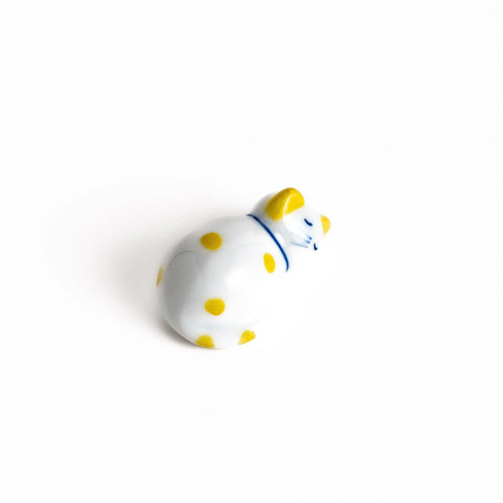 White ceramic cat chopstick rest with yellow dots in sleeping pose adding cheerful touch to dining.