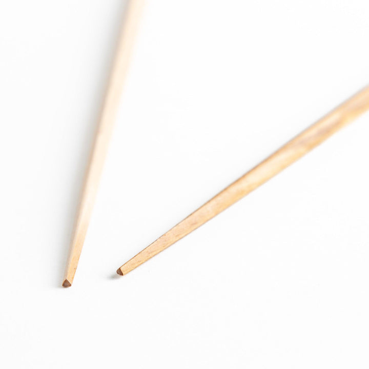 Three pairs of natural chestnut wood chopsticks, each with a different geometric shape—triangle, hexagon, and round.