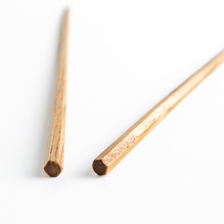 Three pairs of natural chestnut wood chopsticks, each with a different geometric shape—triangle, hexagon, and round.