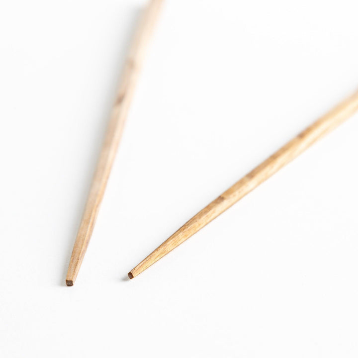 Three pairs of natural chestnut wood chopsticks, each with a different geometric shape—triangle, hexagon, and round.