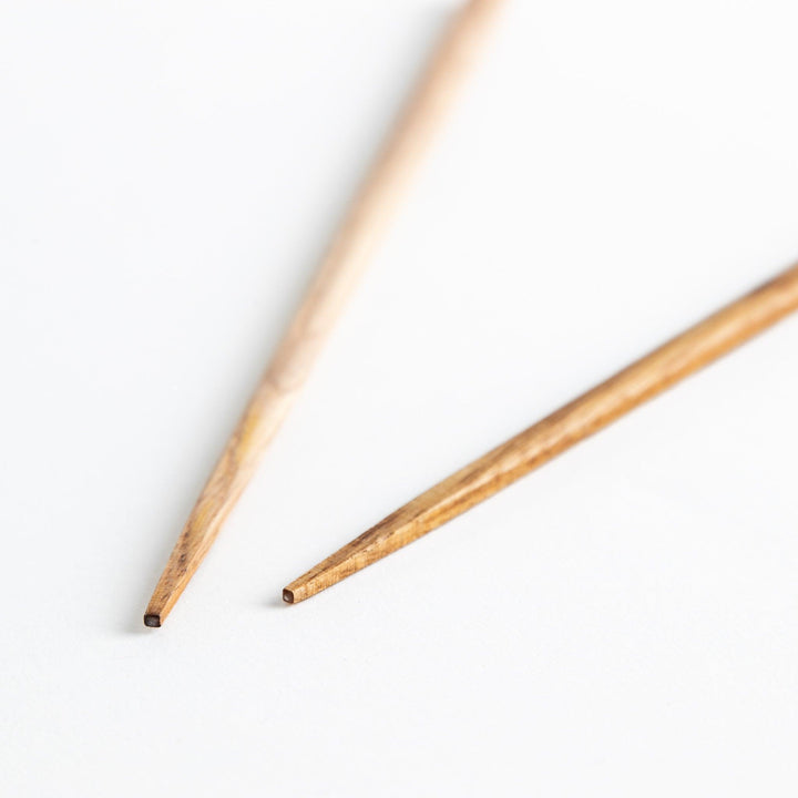 Three pairs of natural chestnut wood chopsticks, each with a different geometric shape—triangle, hexagon, and round.