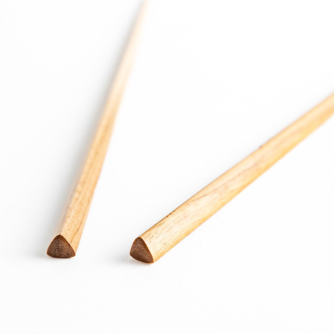 Three pairs of natural chestnut wood chopsticks, each with a different geometric shape—triangle, hexagon, and round.