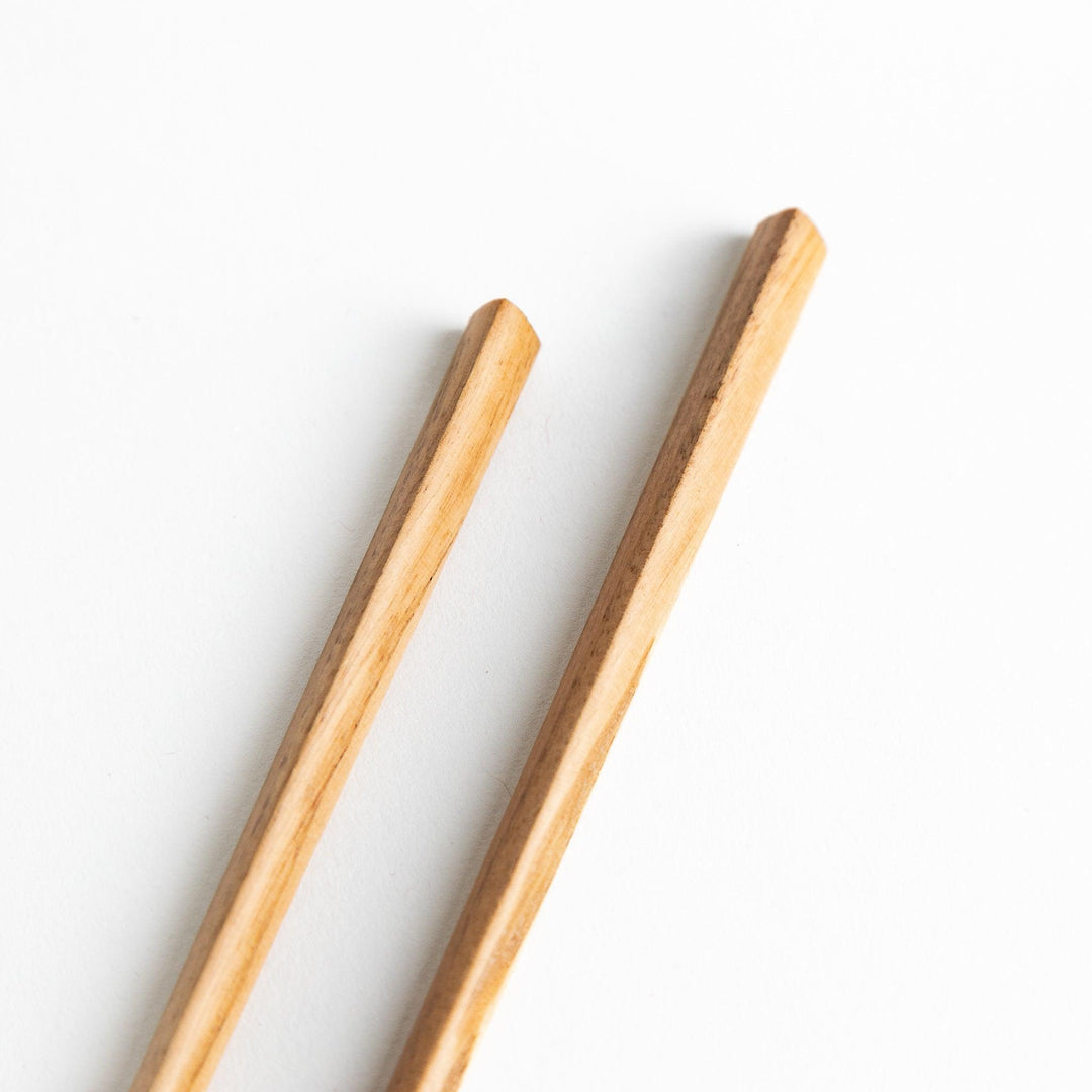 Three pairs of natural chestnut wood chopsticks, each with a different geometric shape—triangle, hexagon, and round.