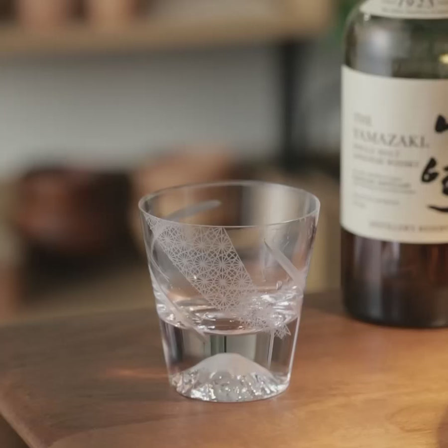 Tajima whiskey cup with whiskey and ice reflecting Mt Fuji peak through carved glass design in light.