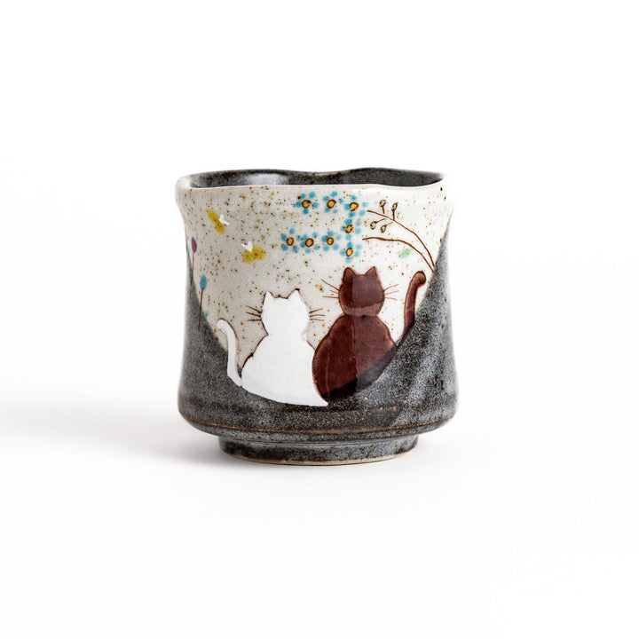 Ceramic teacup with two cats gazing at flowers speckled glaze and gentle shape for cozy tea time.