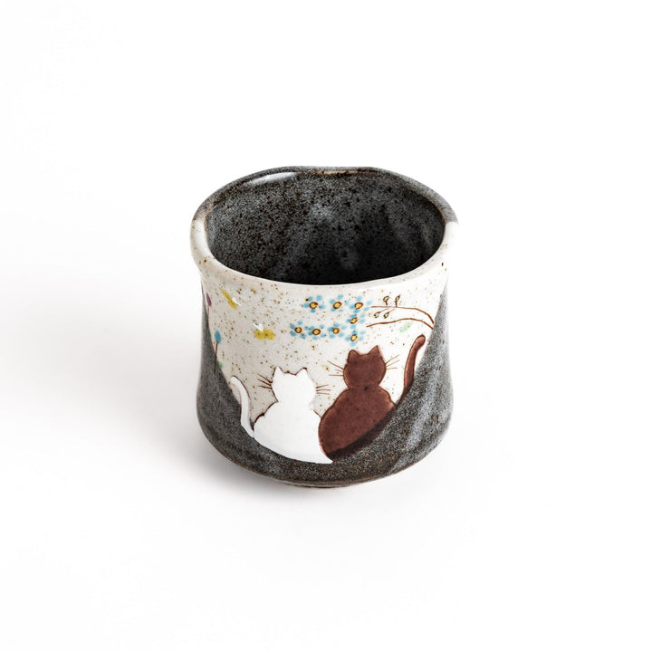 Ceramic teacup with two cats gazing at flowers speckled glaze and gentle shape for cozy tea time.