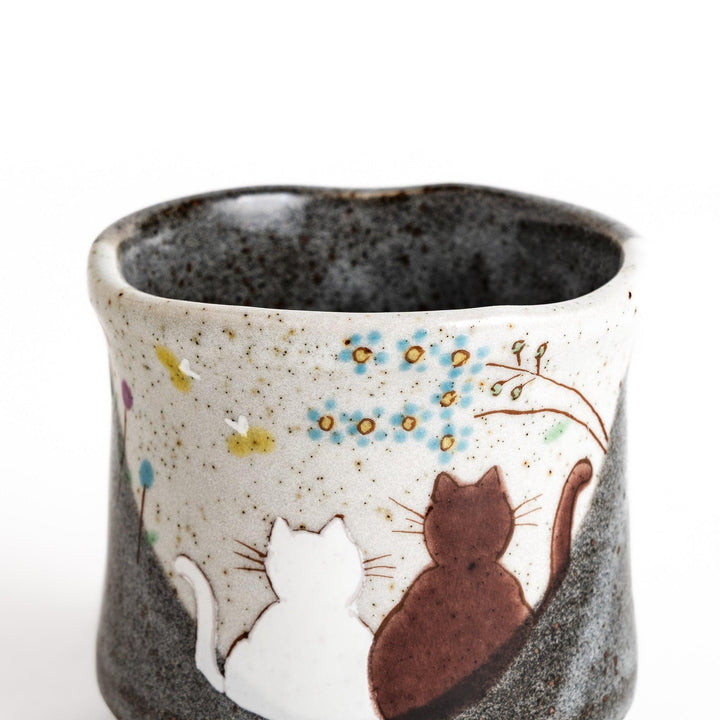 Ceramic teacup with two cats gazing at flowers speckled glaze and gentle shape for cozy tea time.
