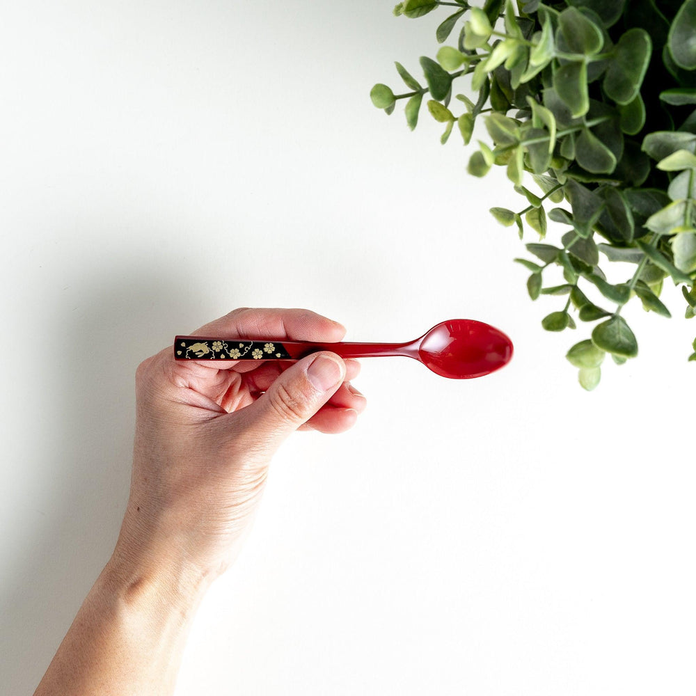 A set of two coffee spoons, one red and one black, with gold floral designs on the handles.