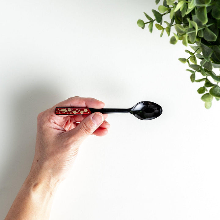 A set of two coffee spoons, one red and one black, with gold floral designs on the handles.