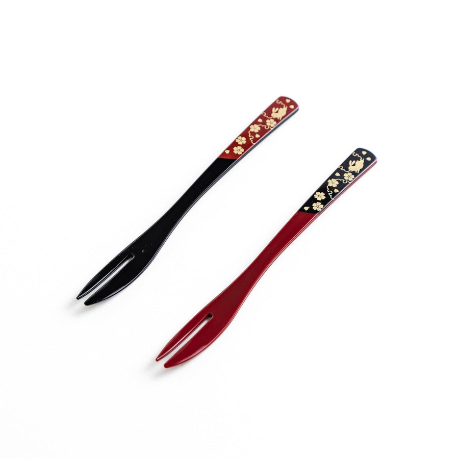A set of two dessert forks, one red and one black, with rabbit designs on the handles.