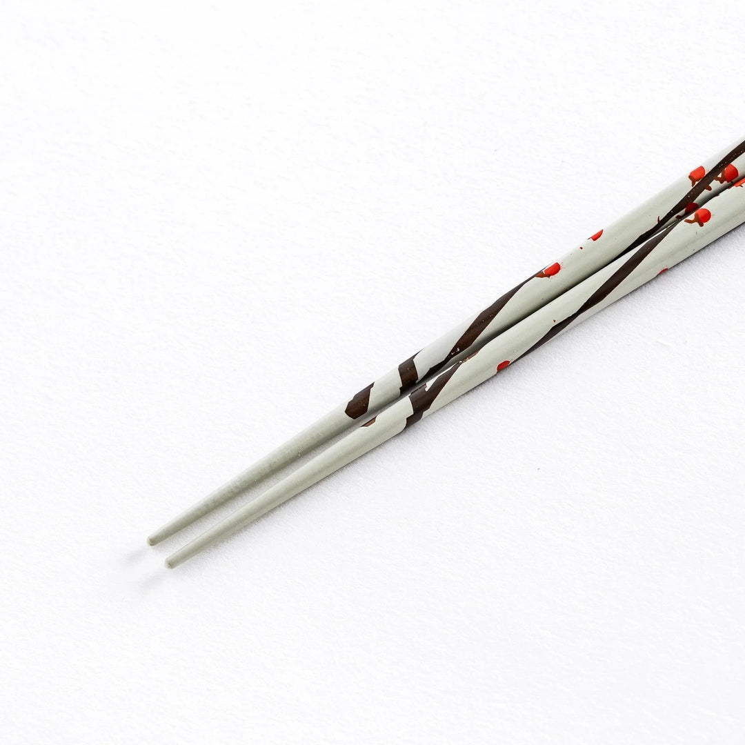 Close-up of the tip of a white chopstick with red plum blossom patterns, highlighting the delicate design.