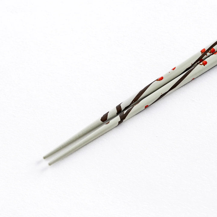 Close-up of the tip of a white chopstick with red plum blossom patterns, highlighting the delicate design.