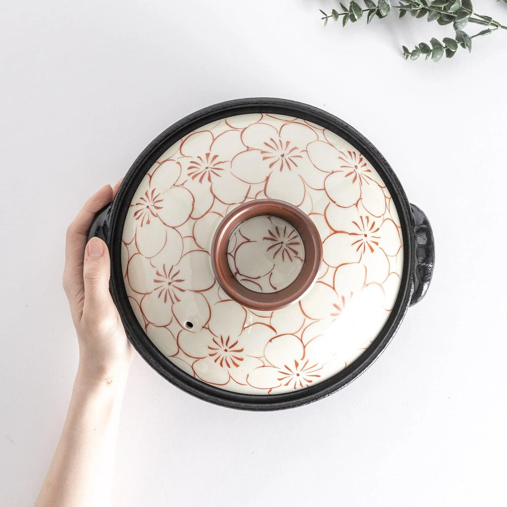 A 8-inch donabe with a vibrant red blossom pattern lid and black pot.